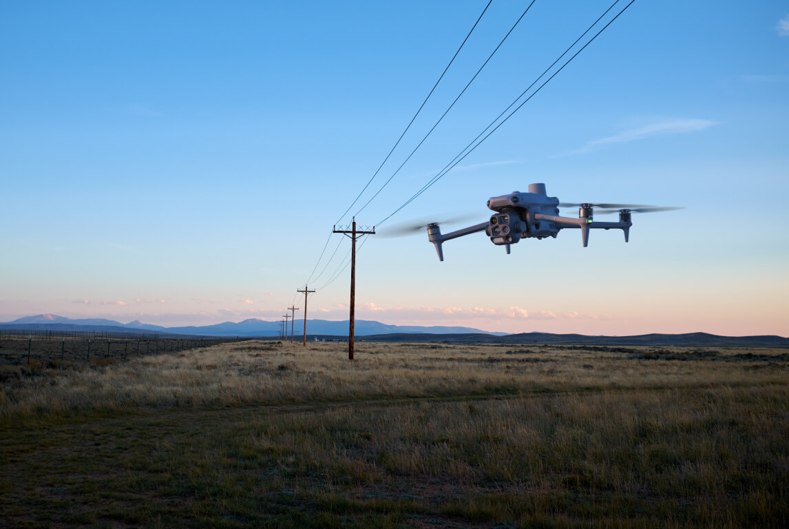 Drone compatto in volo lungo una linea elettrica in area rurale